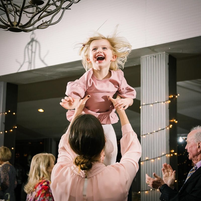Father tosses his daughter in the air at wedding reception as she laughs