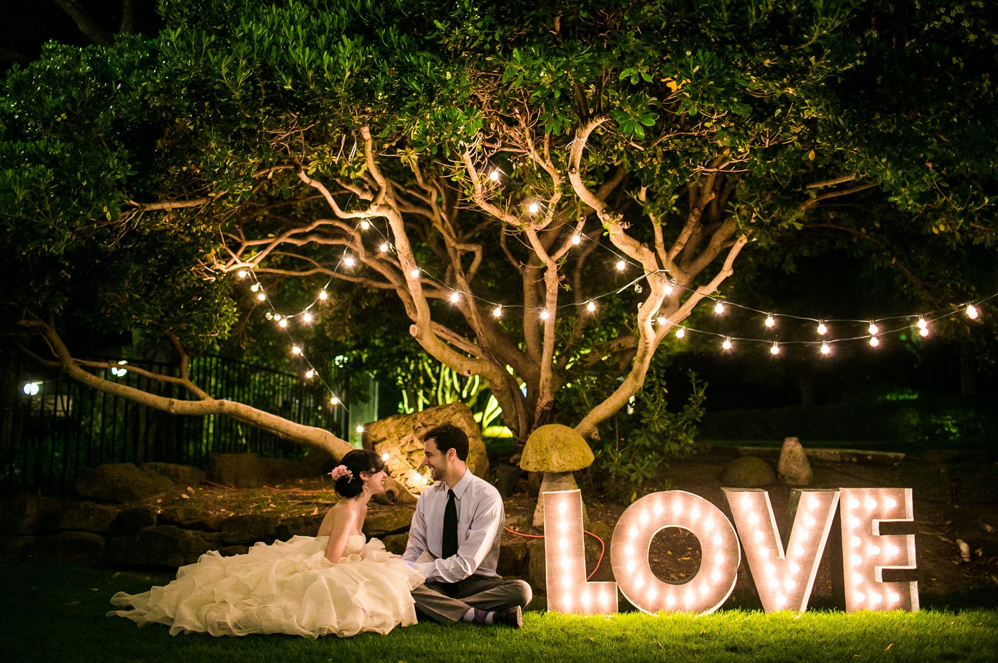 bride and groom sit at night in front of sign that says love