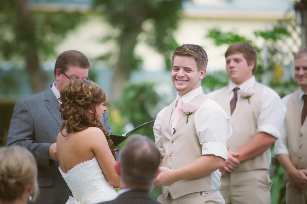 The groom smiles at the bride underneath the large oak tree during their Oak Tree Manor wedding ceremony.