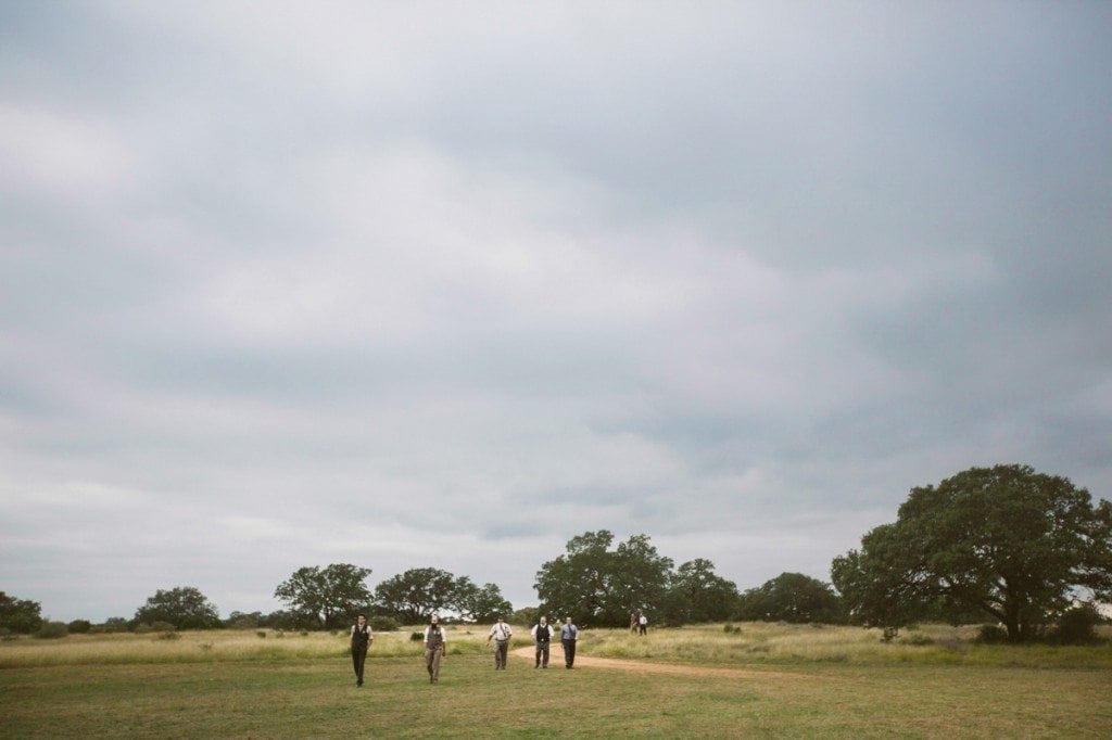 Groomsmen walk through an open field on the way to the wedding ceremony at Three Points Ranch.