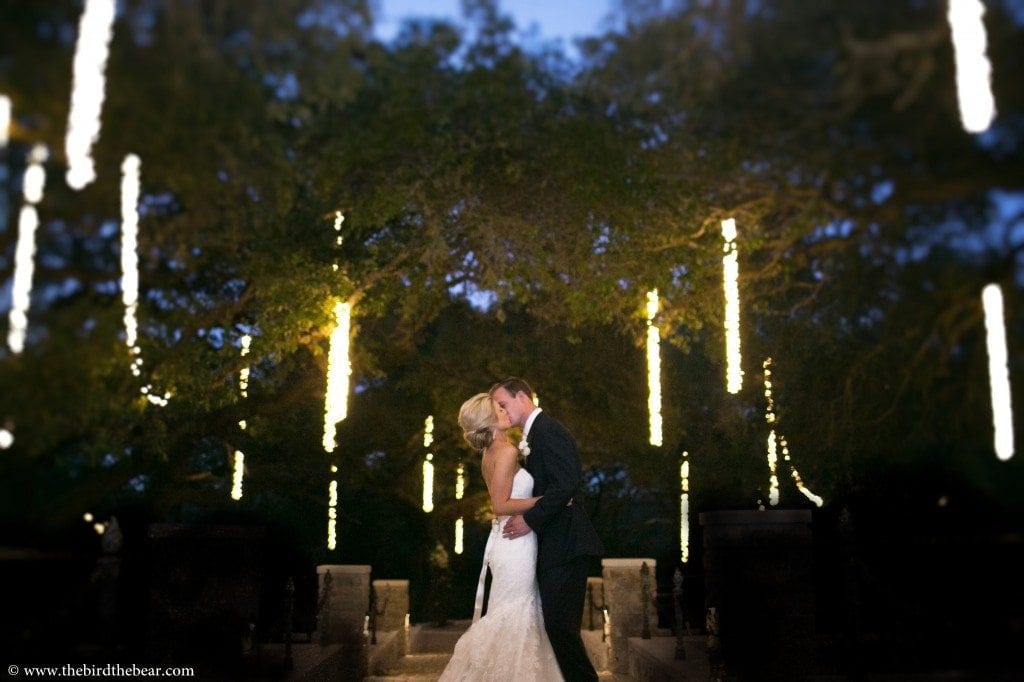 Bride and Groom kiss under the lights at Sacred Oaks at Camp Lucy in Dripping Springs, TX.