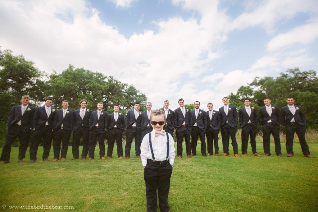 Ring bearer in sunglasses stands in front of all the groomsmen.