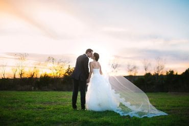 Bride and groom share a kiss as they watch the sun set on the horizon
