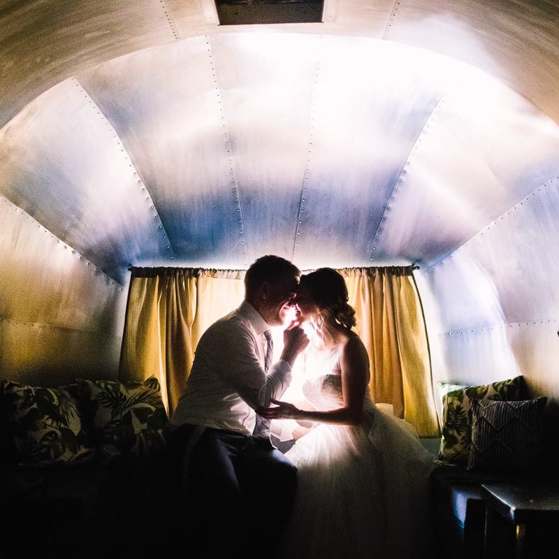 Bride and groom share a kiss at night inside of airstream trailer