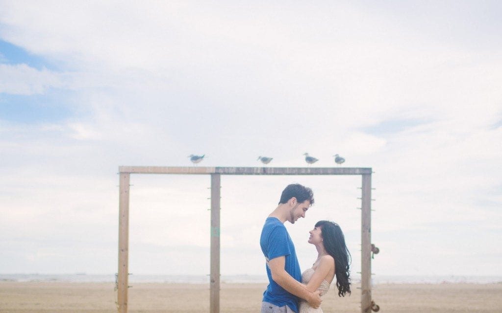 Couple stand under some birds on Stewart Beach in Galveston.