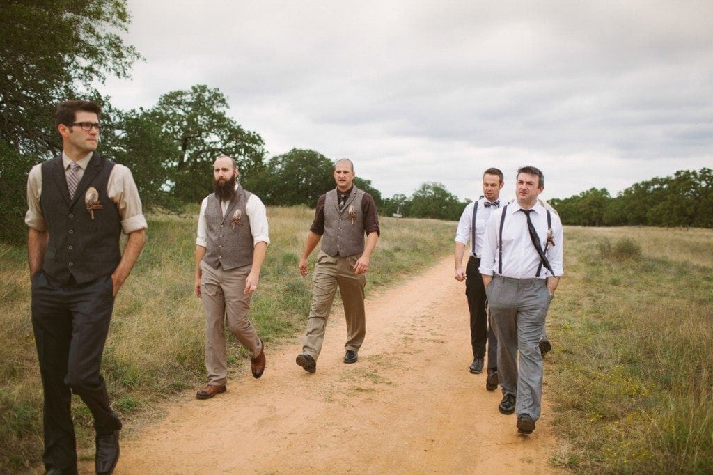 Groomsmen walk down the dirt road between fields at Three Points Ranch wedding venue.