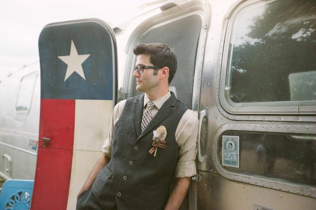 The groom leans on a silver Texas themed airstream trailer at Three Points Ranch.