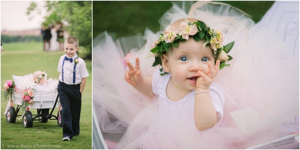 Baby flower girl in a tutu and flower crown rides in a wagon down the aisle, pulled by the ring bearer.