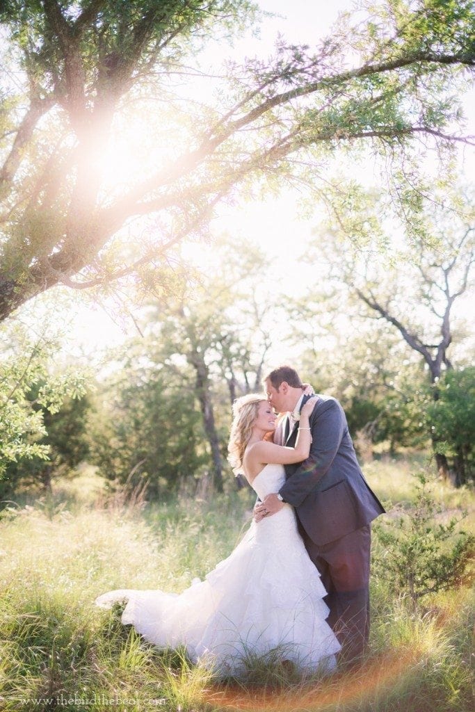 Groom kisses the bride's forehead in a field at sunset during their Vista West Ranch wedding in Dripping Springs, TX.