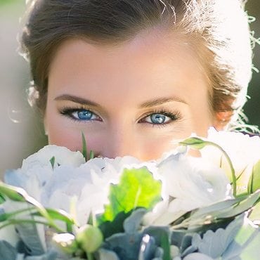 Bride looks over her bouquet of flowers and smiles with her eyes