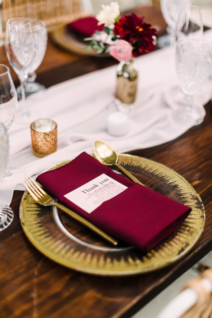 Gold charger with burgundy napkin on table at Maes Ridge wedding reception
